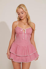 A gingham red tiered mini dress with cami straps and a bow detail at the neckline.