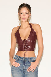 Woman wearing a brown leather halter top and blue jeans against a white background