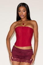 Woman wearing a strapless red top and lace skirt against a plain background
