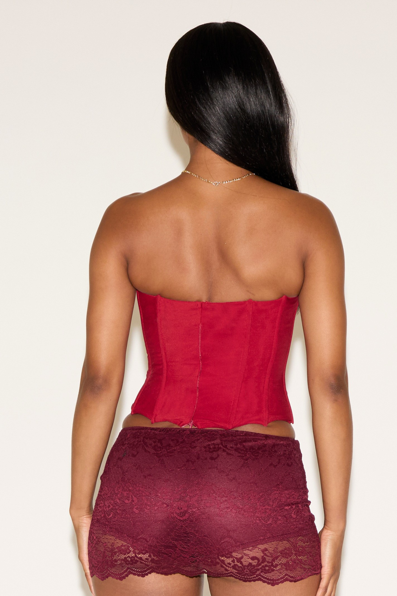 Woman wearing a red strapless top and maroon lace skirt against a white background