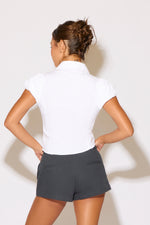 Person wearing a white shirt and gray shorts against a plain background