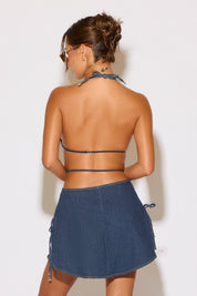 Woman wearing a denim skirt and halter top against a white background