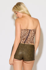 Woman wearing a leopard corset top and leather shorts on a white background