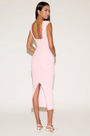 Woman wearing a pink dress with open back and slit on a white background