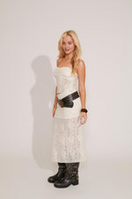 A person wearing a white maxi skirt with a rose pattern and lace detailing, with a white backgrounde background.