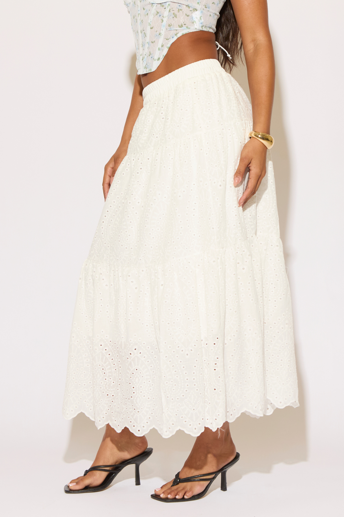 Person wearing a white lace top and long white skirt with black high-heeled sandals on a plain background