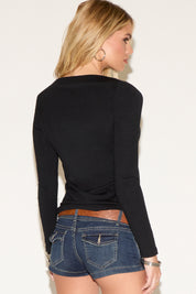 Woman wearing a black long-sleeve top and denim shorts against a plain background