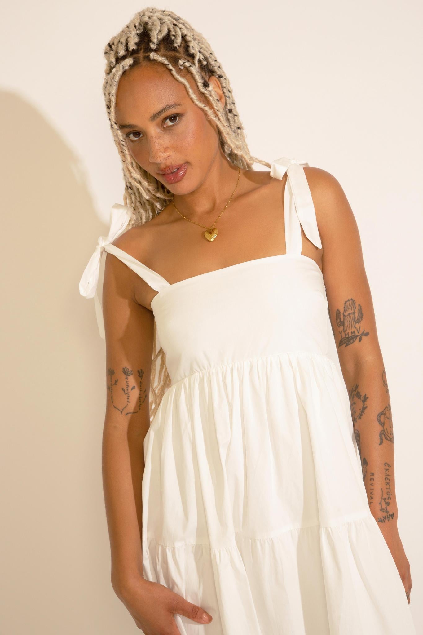 A woman standing wearing a white square neck midi dress with tied straps, a smocked bodice, and an A-line silhouette.