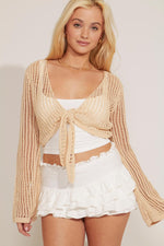 A woman wearing a beige crochet front tie-up cropped top with long sleeves, paired with a white mini skirt.