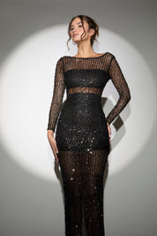 Woman wearing a black sequin dress with sheer long sleeves against a gray background