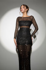 Woman wearing a black sequin dress with sheer long sleeves against a gray background