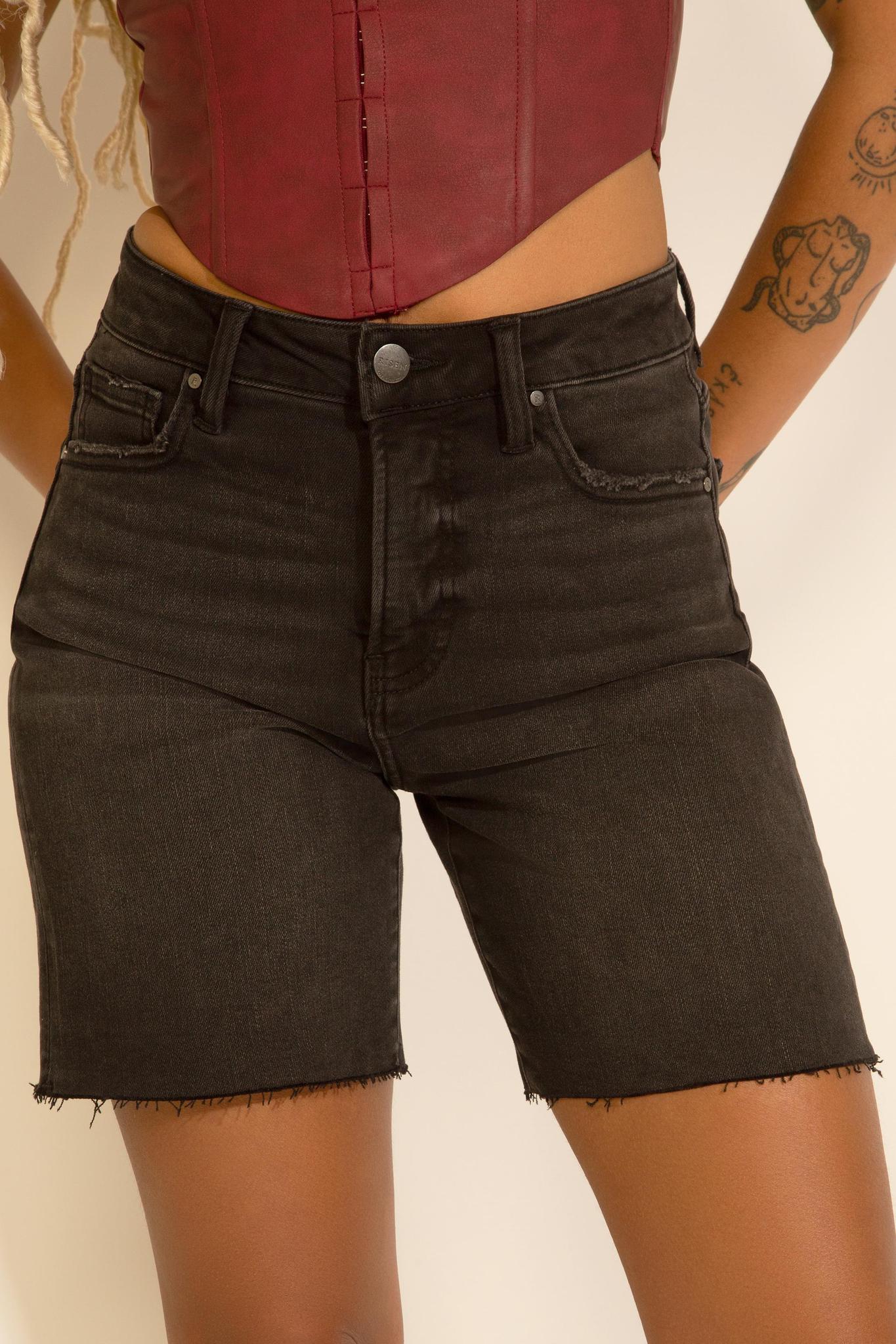 Model is wearing tummy control high rise mid length black denim shorts with a burgundy top on a white background. 