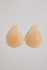 Pair of beige silicone bra cups on a light gray background