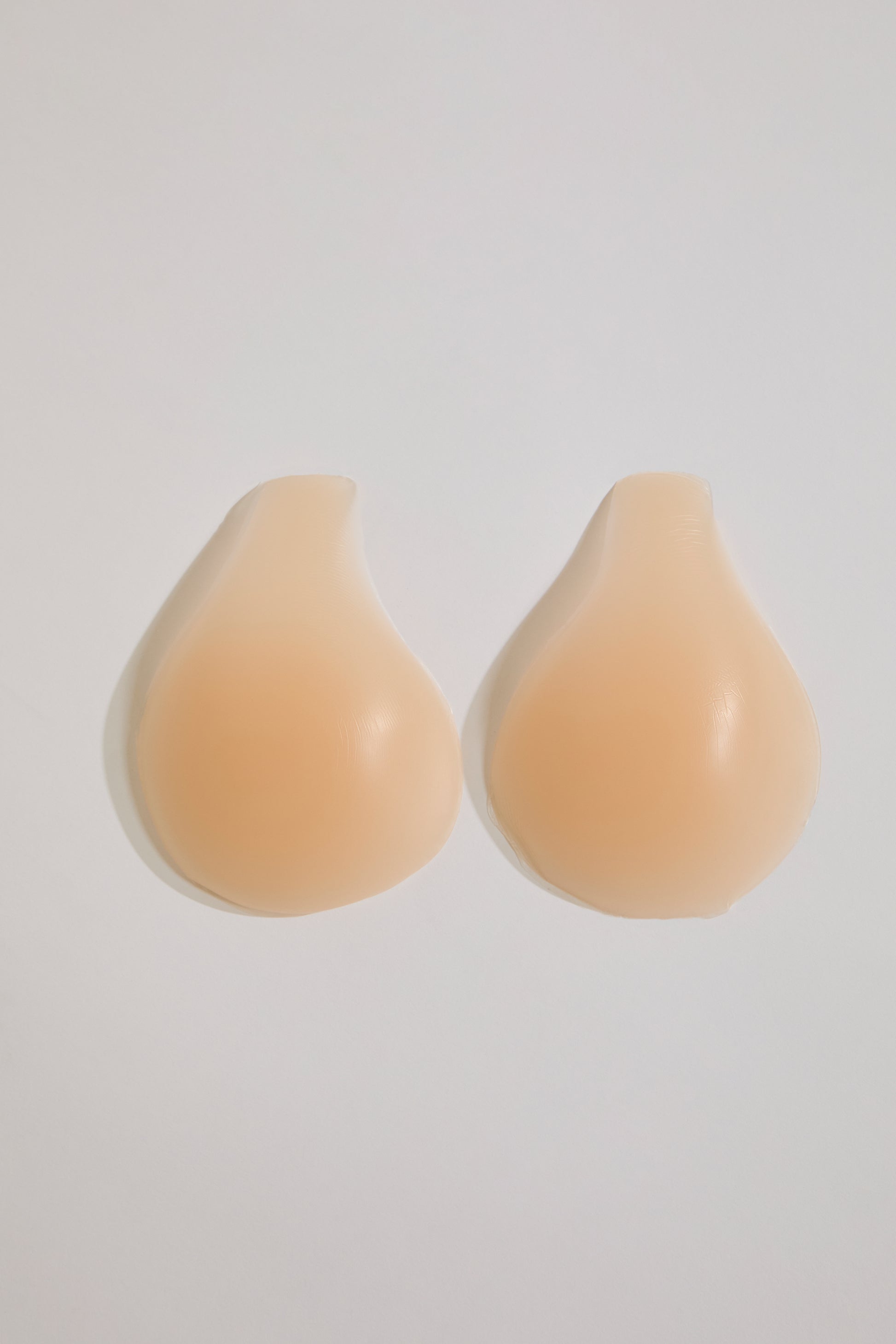 Pair of beige silicone bra cups on a light gray background