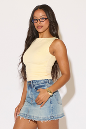 Woman wearing a yellow top and denim skirt against a white background
