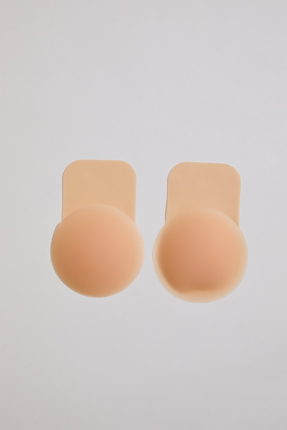 Two beige silicone bra cutlets on a light gray background
