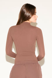 Woman wearing a brown long-sleeve top and pants against a white background