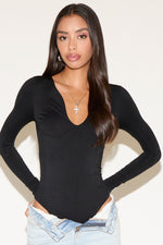 Woman wearing a black long-sleeve top and light blue jeans against a white background