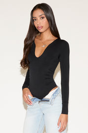 Woman wearing a black long-sleeve top and light blue jeans against a white background