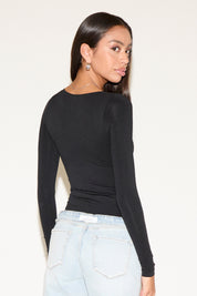 Woman wearing a black long-sleeve top and light blue jeans against a white background