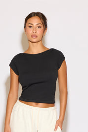 Woman wearing a black top and white pants against a plain background