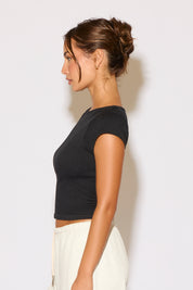 Woman wearing a black crop top and white pants against a plain background