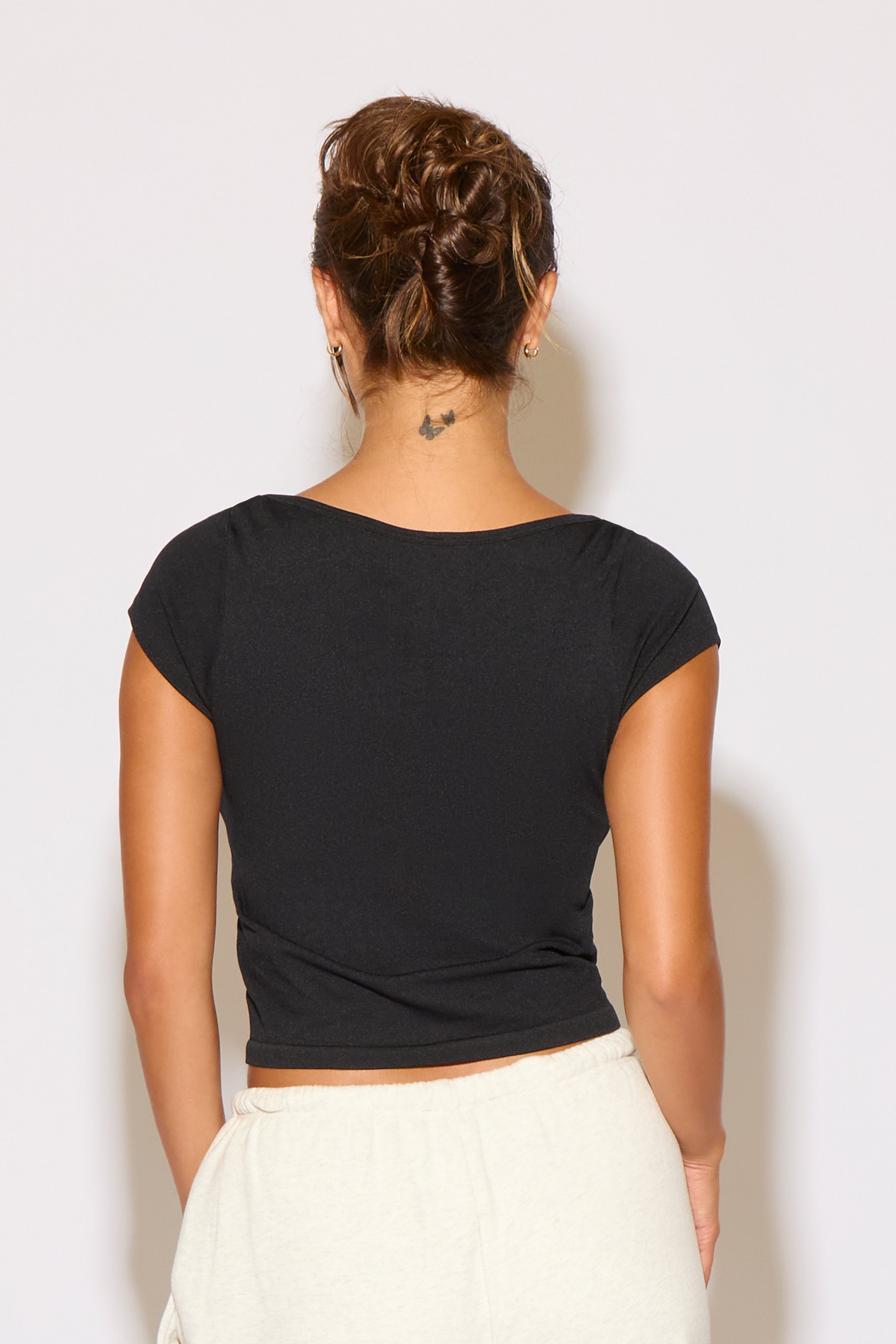 Person wearing a black crop top and white pants against a plain background
