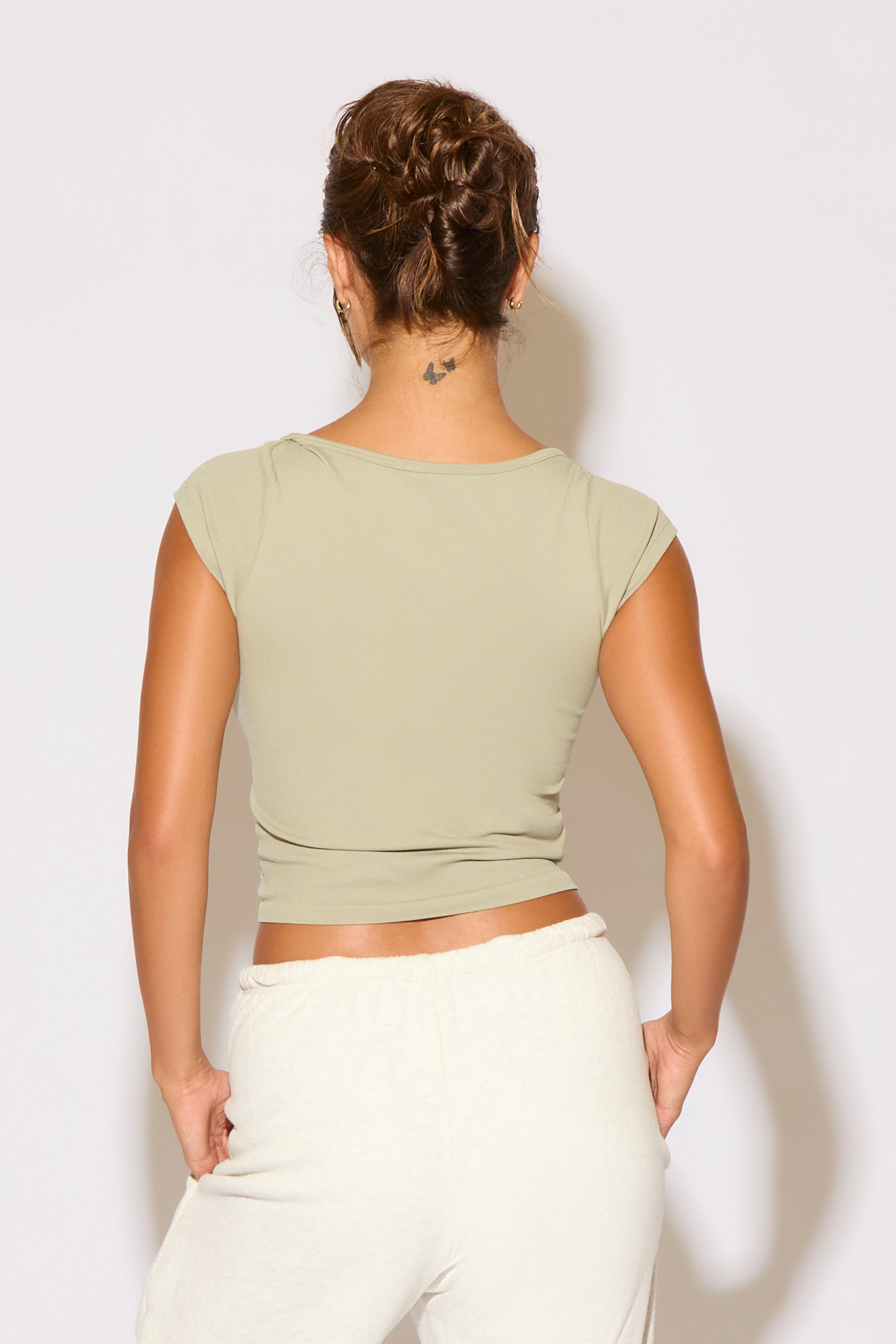 Person wearing a green crop top and white pants against a light background