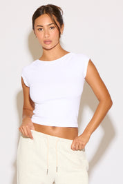Woman wearing a white crop top and light-colored pants against a plain background