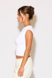 Woman wearing a white sleeveless top and light-colored pants against a plain background