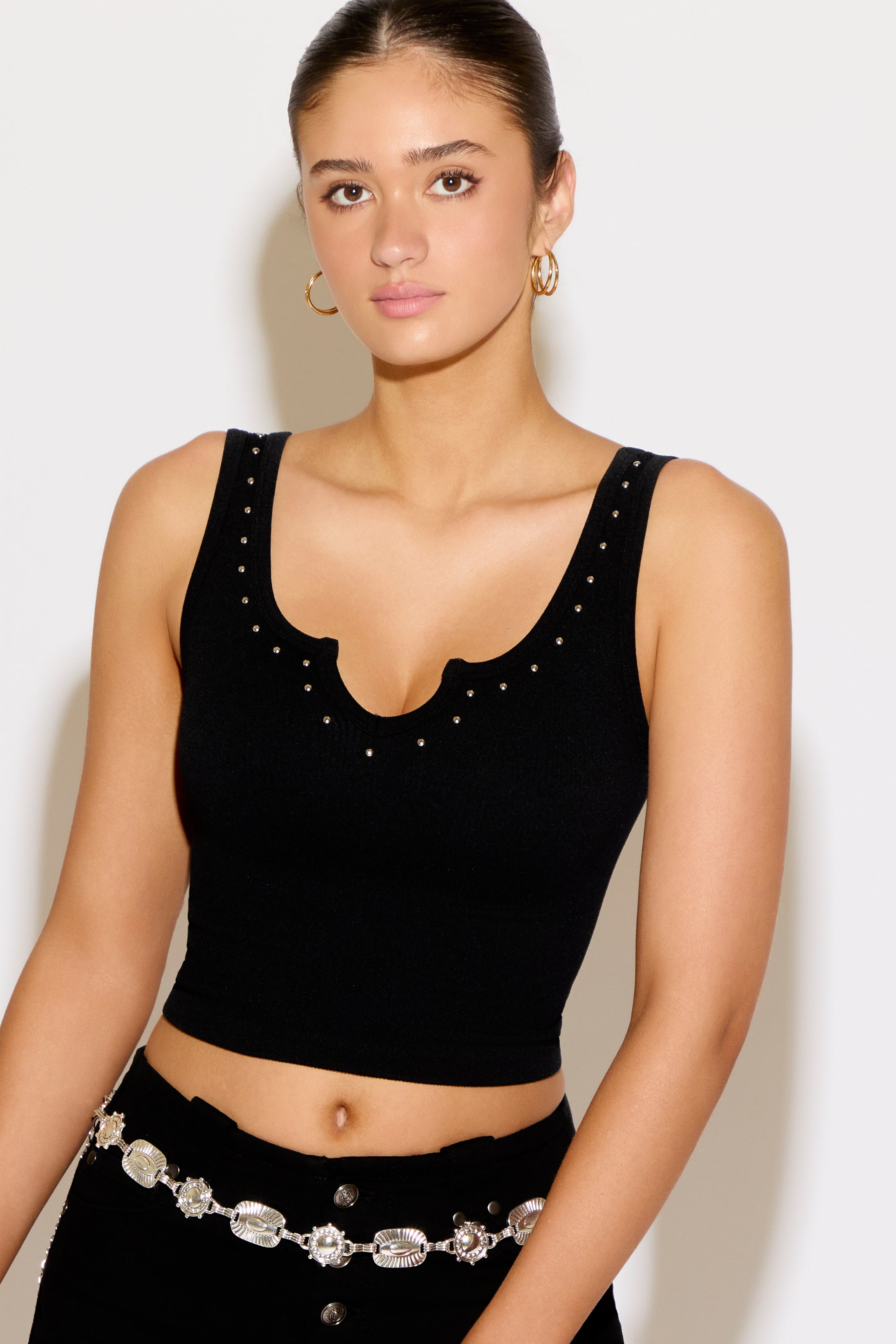 Woman wearing a black sleeveless top with embellishments on a white background