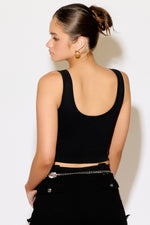Woman wearing a black tank top and pants against a white background