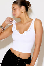 Woman wearing a white tank top with embellishments against a plain background
