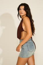 Woman in brown halter top and denim shorts against a plain background