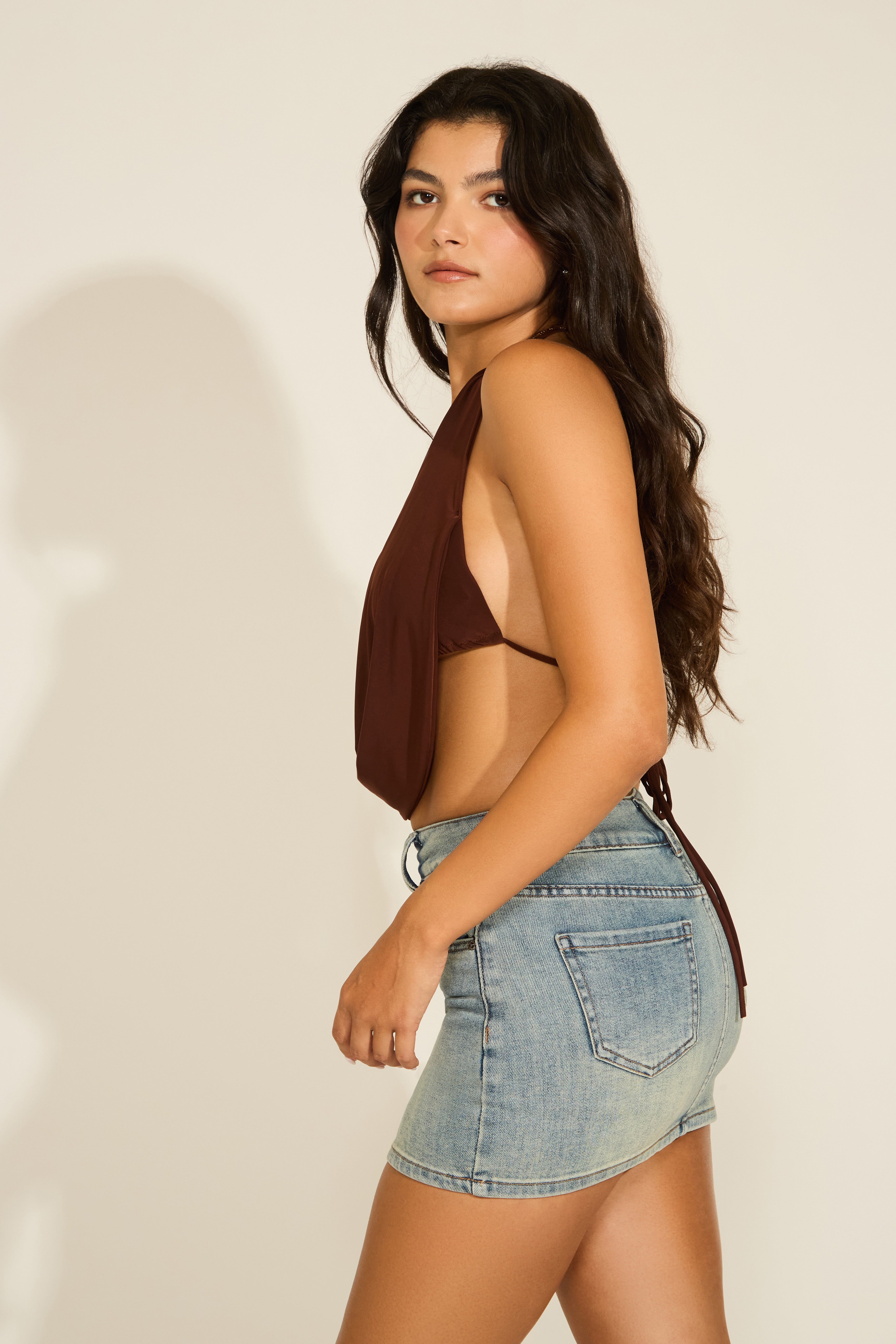 Woman in brown halter top and denim shorts against a plain background