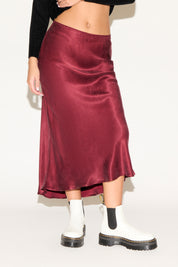 Person wearing a burgundy satin skirt with white socks and black boots on a plain background