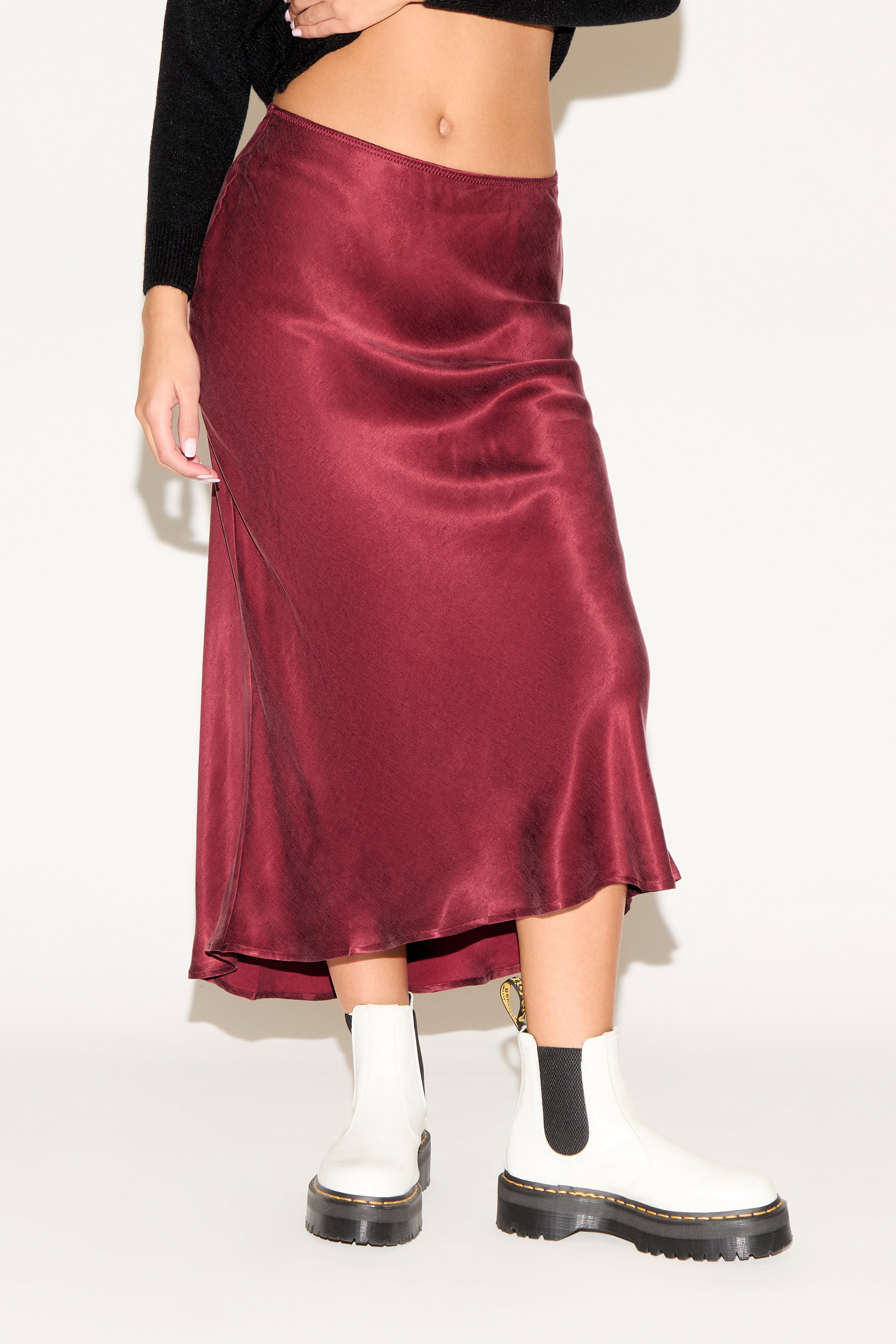 Person wearing a burgundy satin skirt with white socks and black boots on a plain background