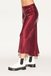 Person wearing a burgundy satin skirt with white boots on a white background