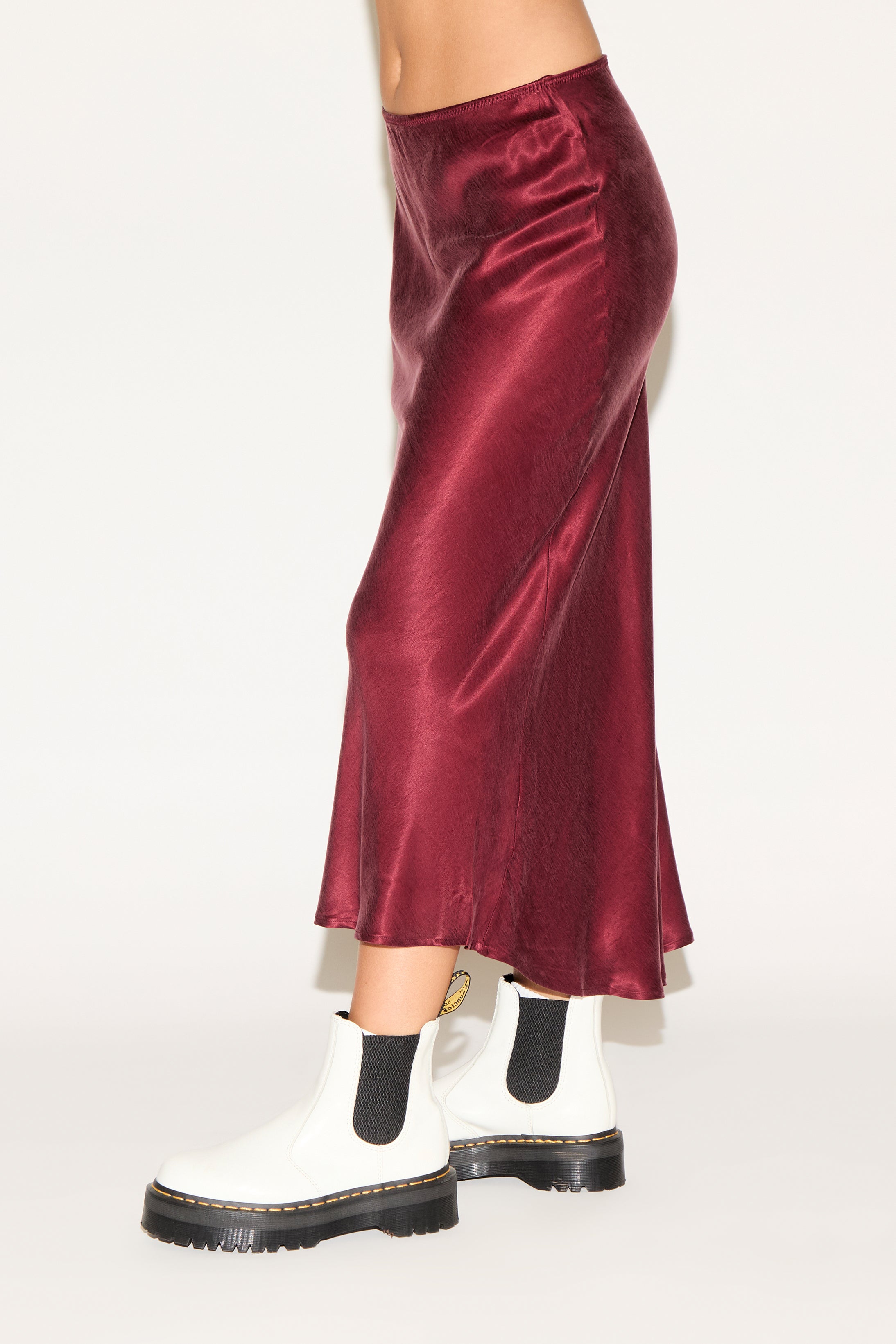 Person wearing a burgundy satin skirt with white boots on a white background
