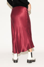 Person wearing a burgundy satin skirt with black shoes on a white background