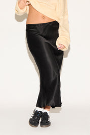 Person wearing black satin pants with a plain background
