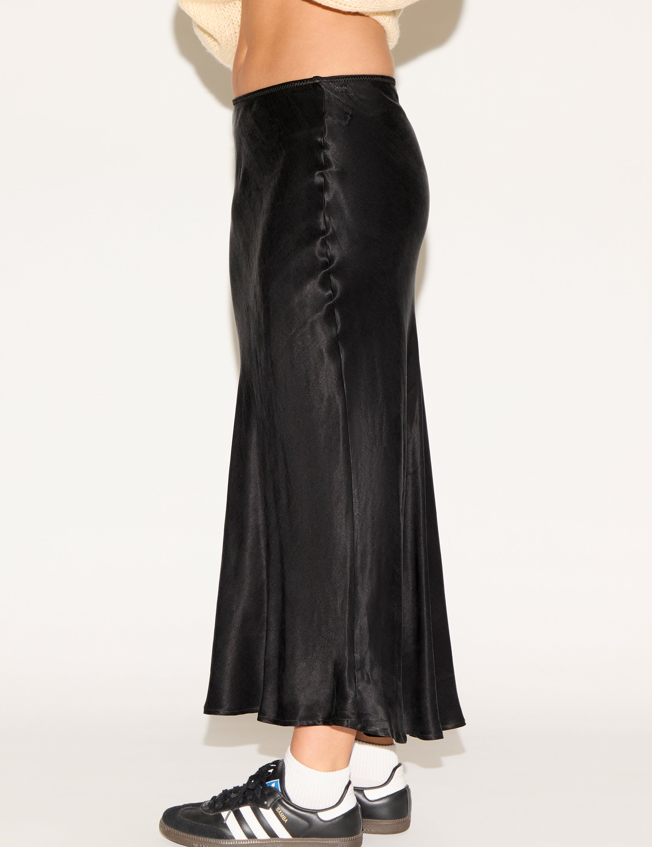 Person wearing a black satin skirt with a plain background