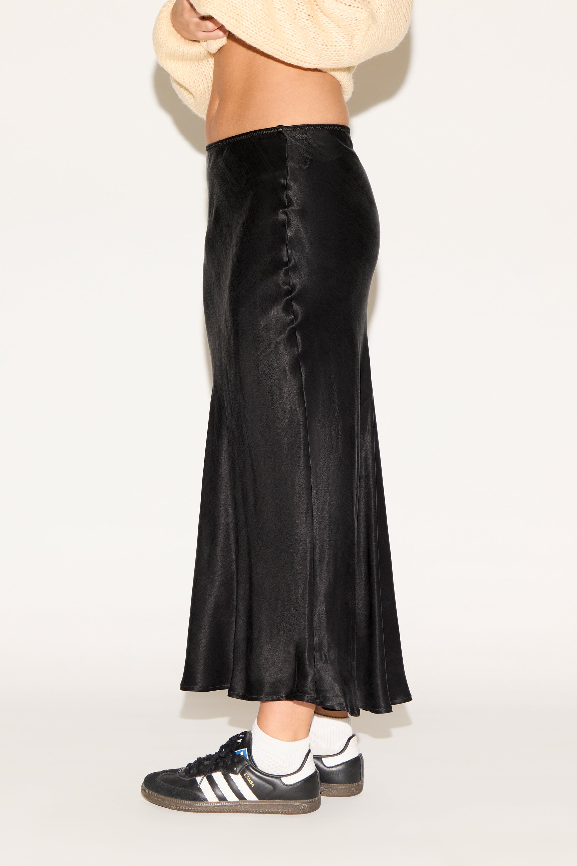 Person wearing a black satin skirt with a plain background