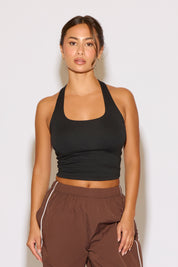 Woman wearing a black halter top and brown pants against a white background