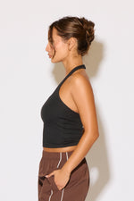 Woman wearing a black crop top and brown pants against a white background