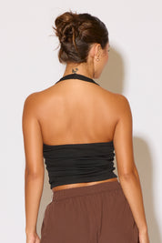 Woman wearing a black halter top and brown pants against a white background