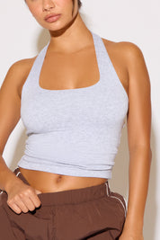 Person wearing a light grey tank top and brown pants against a white background