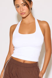 Woman wearing a white halter top and brown pants against a plain background