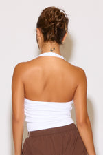 Person wearing a white strapless top and brown pants against a plain background