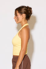Woman wearing a yellow top and brown pants against a white background